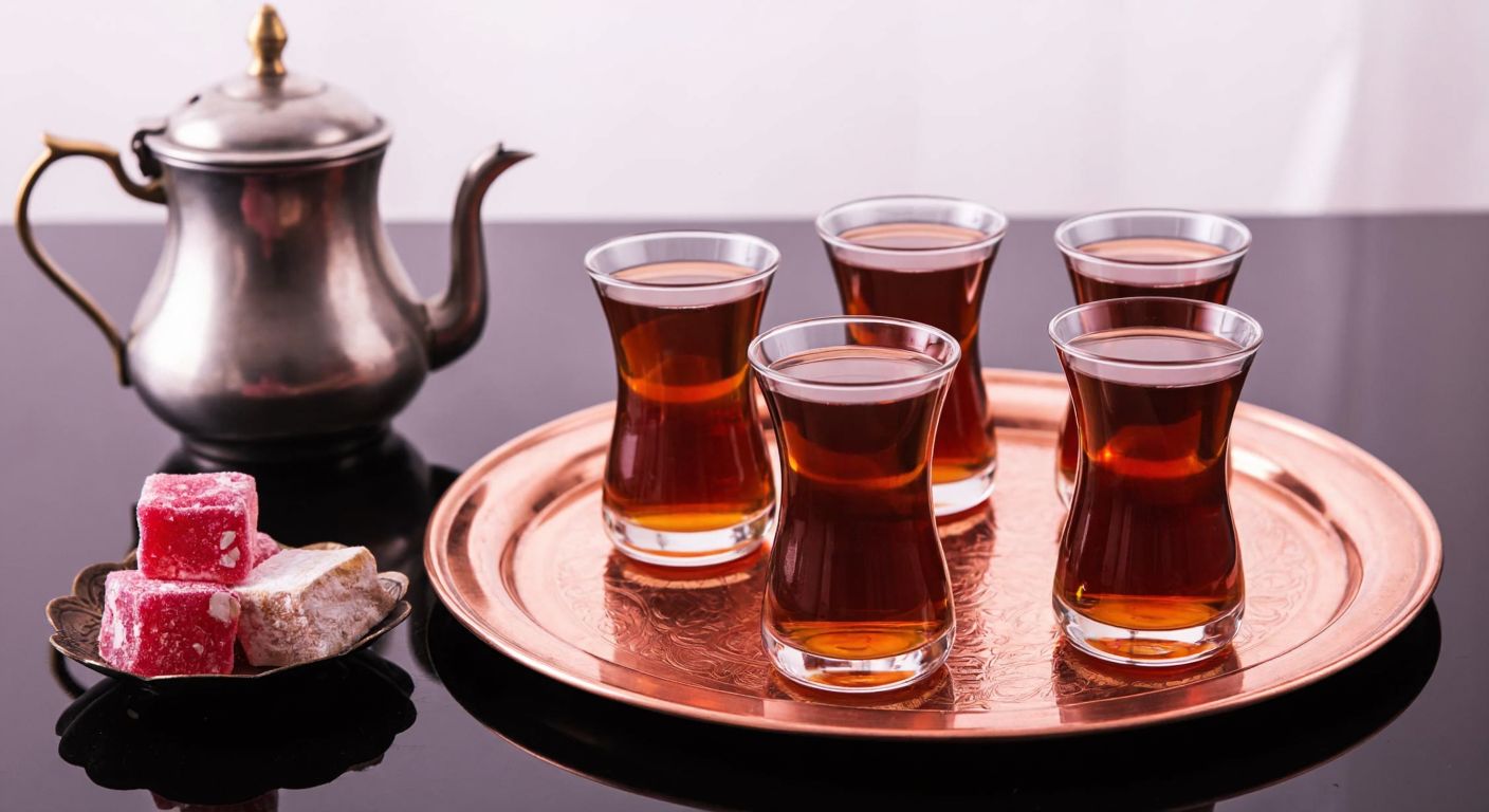 A traditional Turkish tea set with four delicate, tulip-shaped glass cups (320 cc each) placed on a copper tray, accompanied by a steaming teapot and a small plate of Turkish delight, evoking warmth and hospitality.