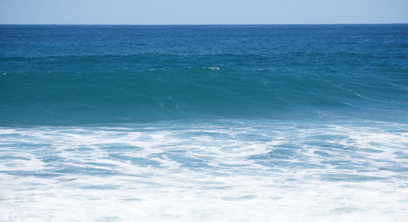 A serene blue ocean with gentle waves rolling toward the shore, their peaks and troughs clearly visible, symbolizing wavelength and frequency in nature.