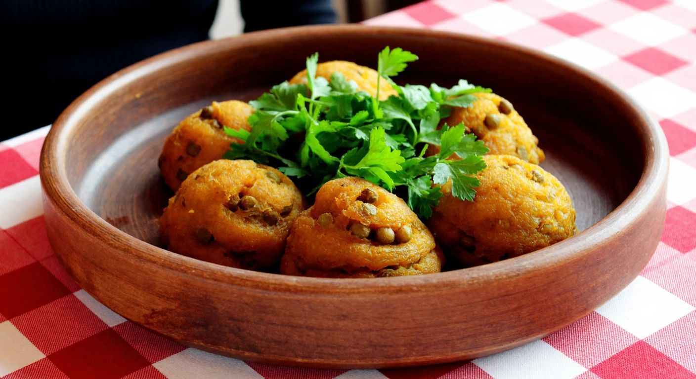 A rustic wooden bowl filled with warm, golden-brown galacoş made with green lentils, garnished with fresh parsley, placed on a checkered tablecloth in a cozy Turkish kitchen.