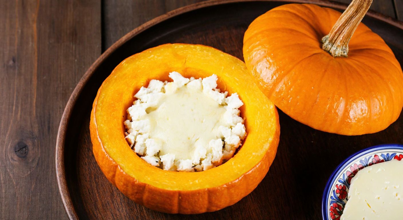 A golden roasted pumpkin, sliced open to reveal a warm, melted filling of crumbled white cheese and stretchy kaşar cheese, resting on a rustic wooden table with a traditional Turkish ceramic plate nearby.