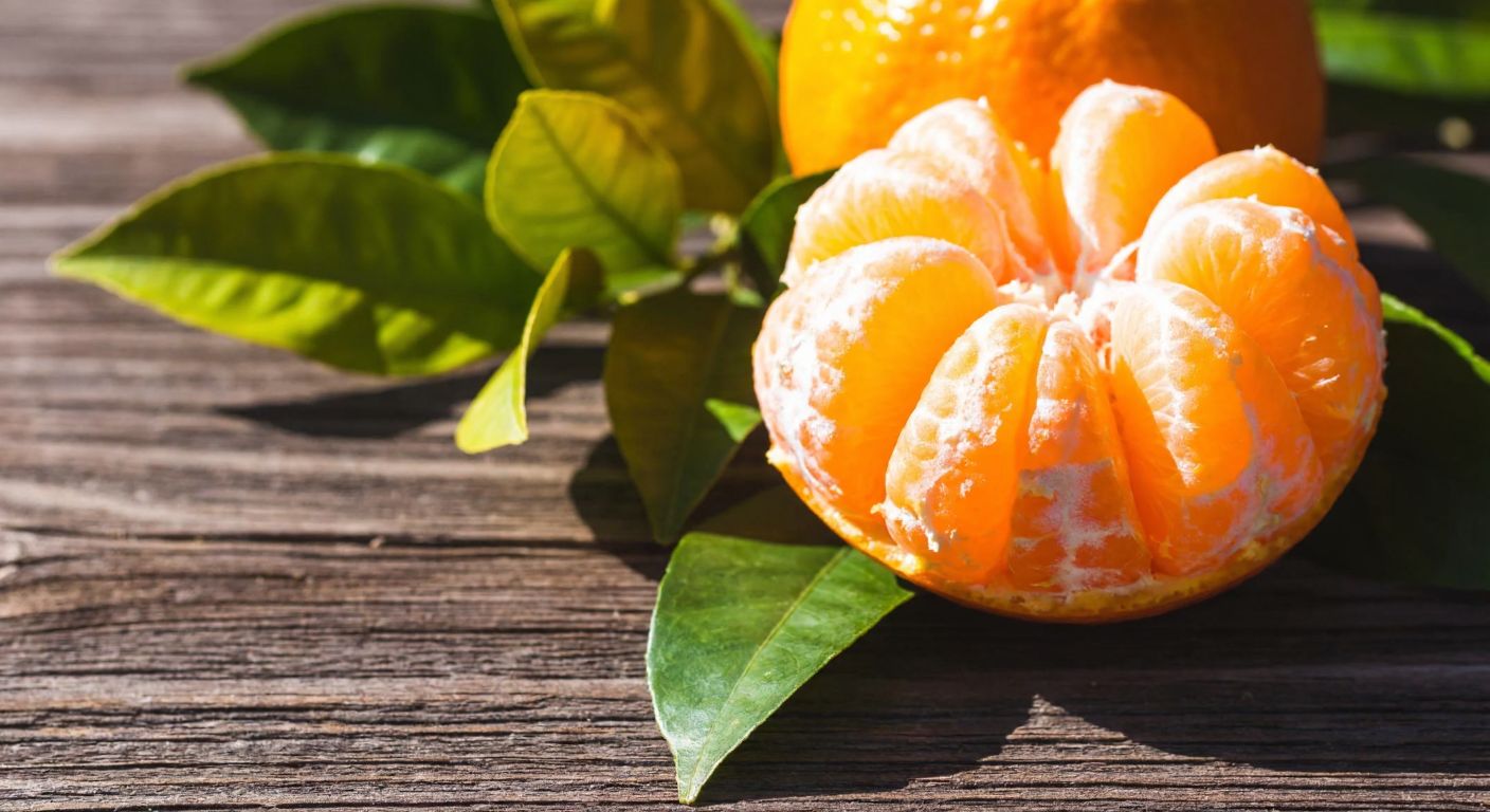 A vibrant, freshly peeled orange with juicy segments resting on a rustic wooden table, surrounded by sunlit citrus leaves, evoking freshness and health.