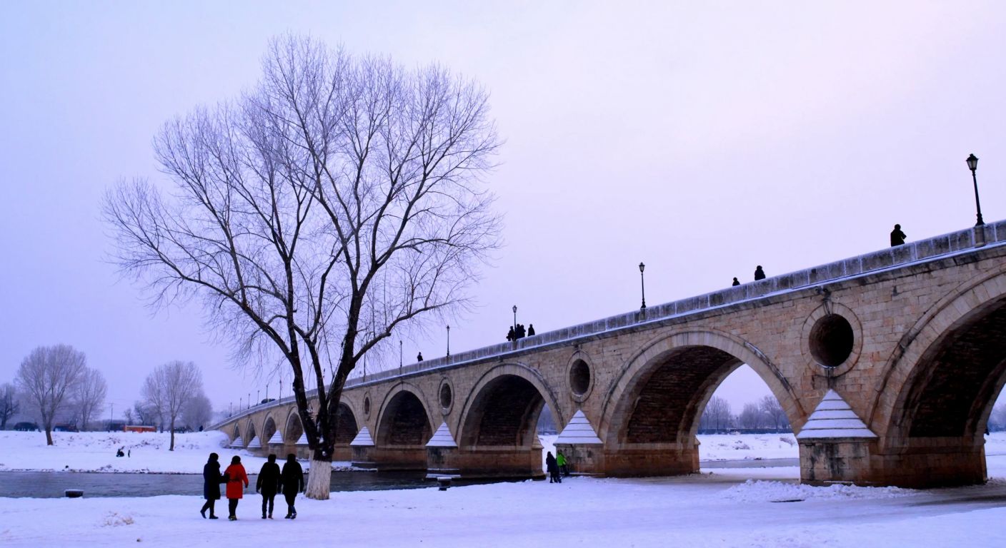 A frost-covered historic bridge in Edirne under a pale winter sky, with bare trees and people bundled in thick coats, their breath visible in the icy air.