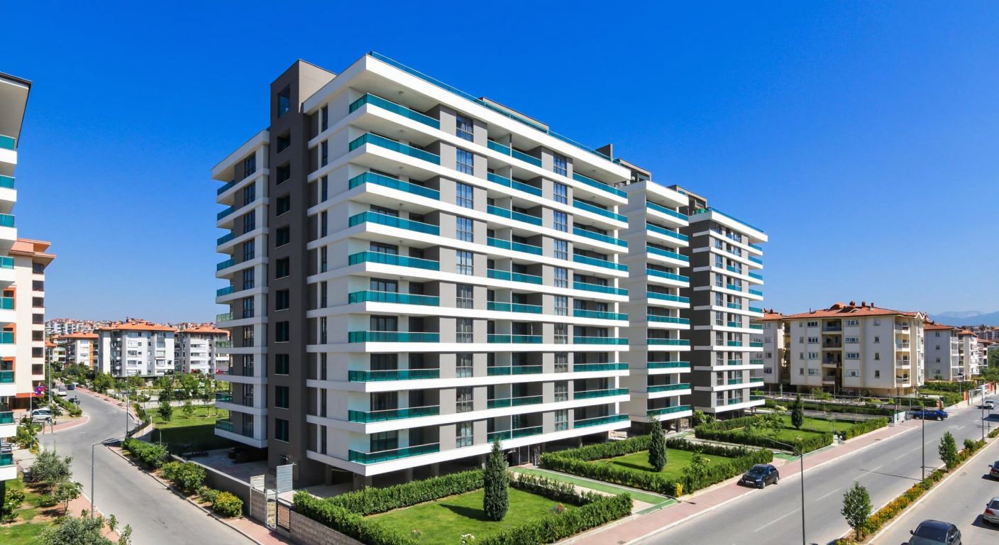 A modern high-rise apartment building with numerous identical balconies under a clear blue sky, surrounded by neatly landscaped gardens and a bustling urban neighborhood in Turkey.