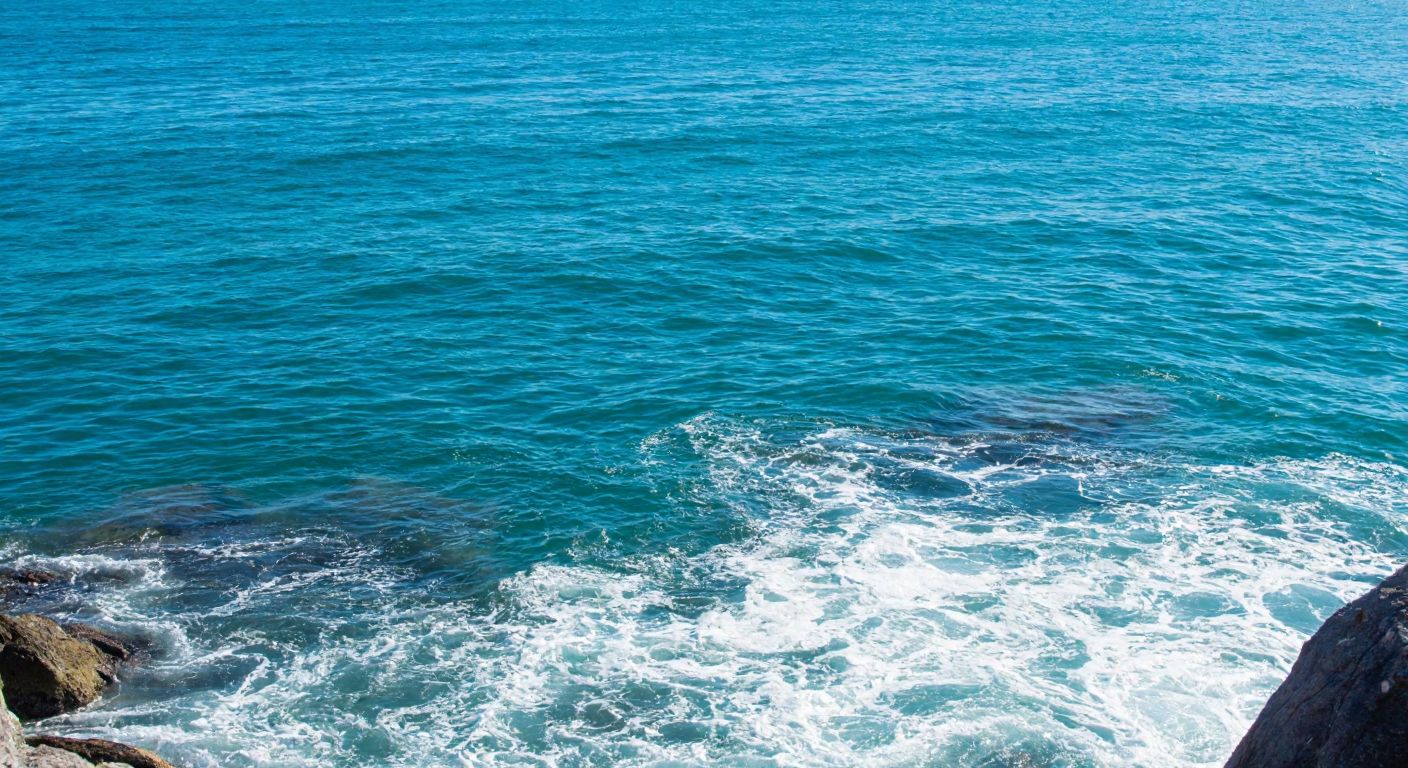 A serene turquoise sea with gentle waves lapping against a rocky shore, while sunlight reflects off the water’s surface, illustrating both transverse and longitudinal wave motion.