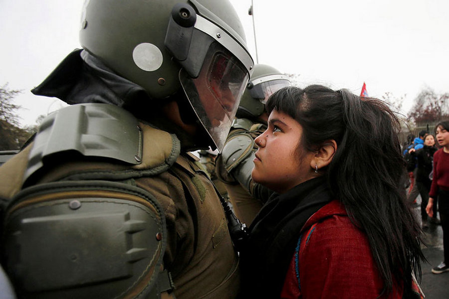 Участница демонстрации смотрит на полицейского во время акции протеста в Сантьяго, Чили, 11 сентября.