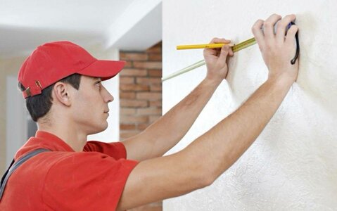 человек измеряет рулеткой толщину стены в комнате