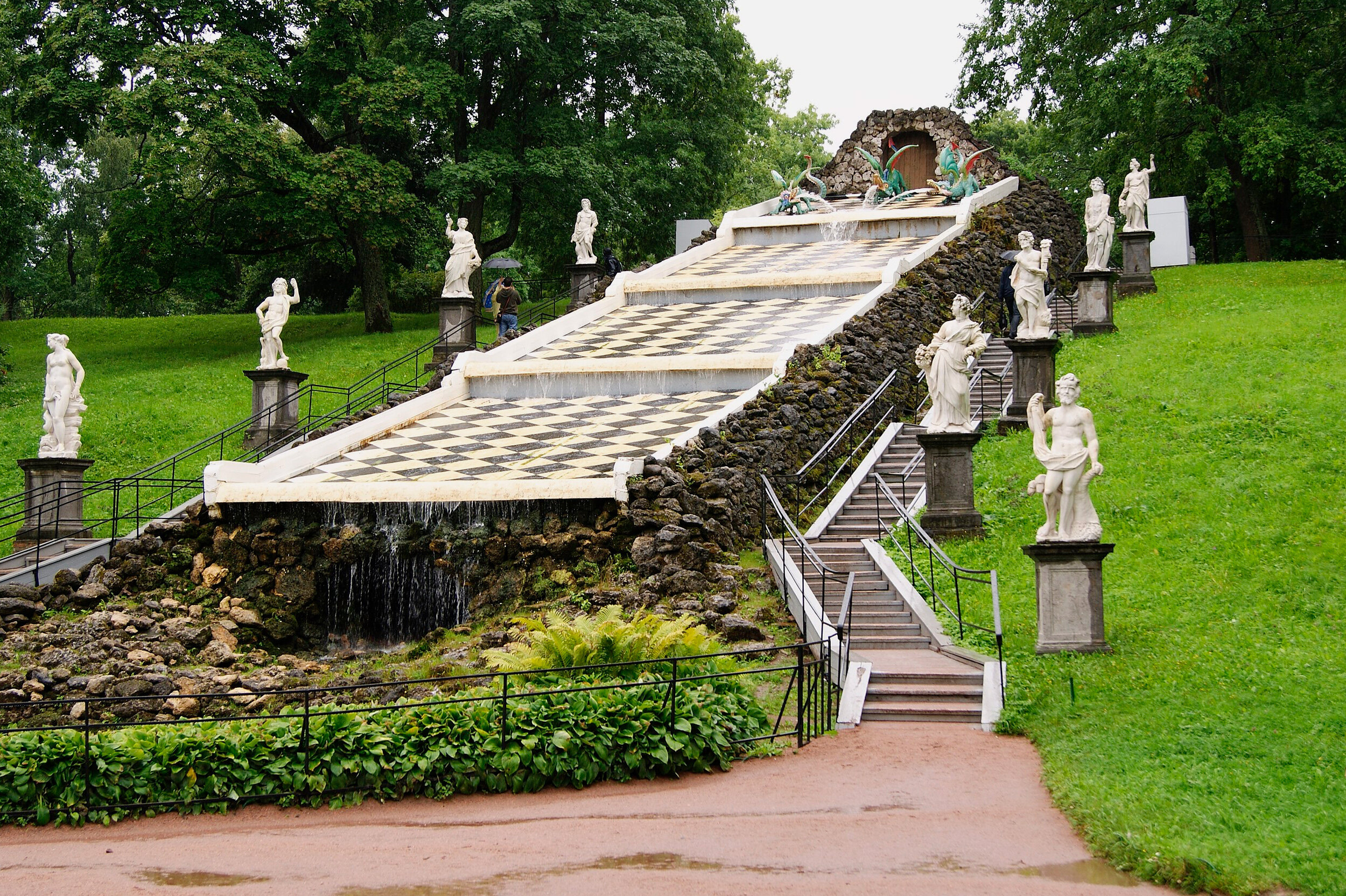 По двум сторонам фонтана наверх ведут лестницы, рядом с которыми выстроены каменные пьедесталы с белыми мраморными скульптурами десяти античных богов.