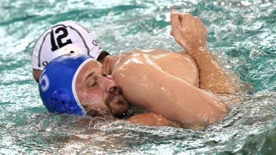 напряженный момент матча по водному поло, брызги воды, спортсмены в шапочках борются за мяч