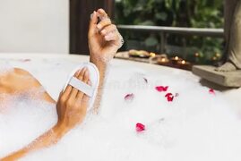 Ноги женщины моя в ванне с пузырями пены и использовать естественную губку люфы Стоковое Фото - изображение насчитывающей здоров