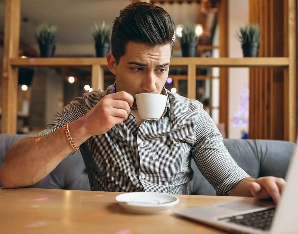 Парень пьет кофе. Мужик с чашкой кофе. Мужчина за столиком в кафе. Люди в кофейне. Вечерний подработка для мужчин