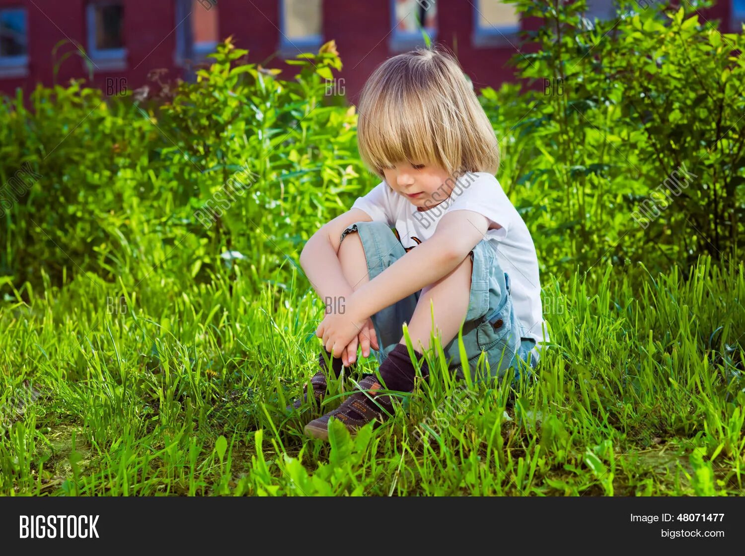 Скука на даче. Мальчик сидит на траве. Малыш сидит на траве. Мальчик на травке. Грустный мальчик.