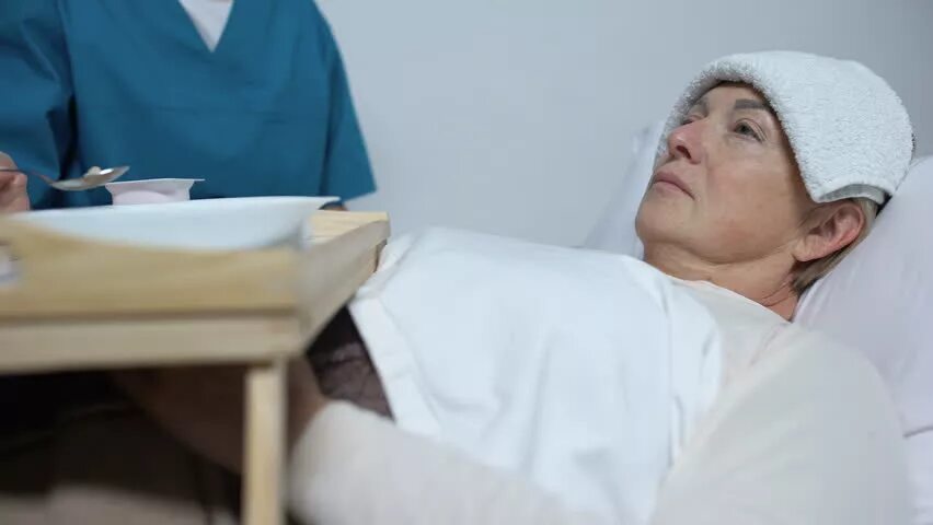 Пациент лежит. Холодный компресс на лоб. Медсестра и лежачий пациент.