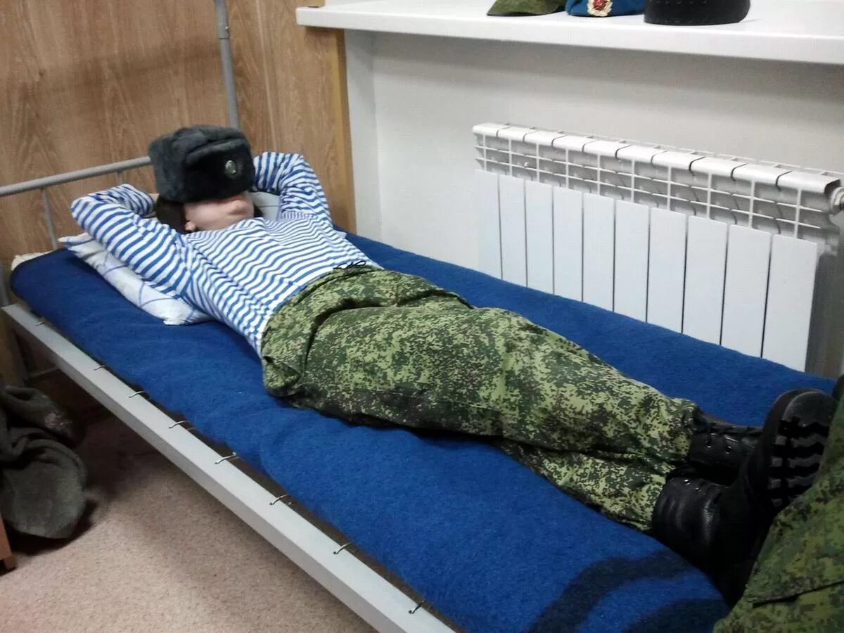 Солдат со спины. Солдаты спят в военной форме. Кровати в казарме.
