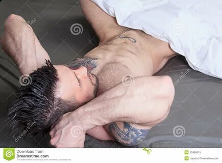 Foto acerca Un hombre desnudo atractivo con el tatuaje pone en la cama. 