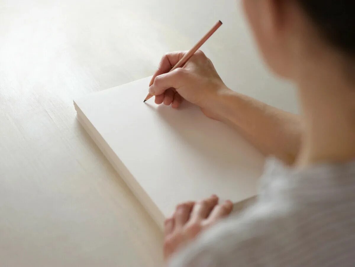 Человек пишет на листе бумаги. Пишет на бумаге. Лист бумаги на столе. Бумага в руке. Девушка пишет на бумаге.