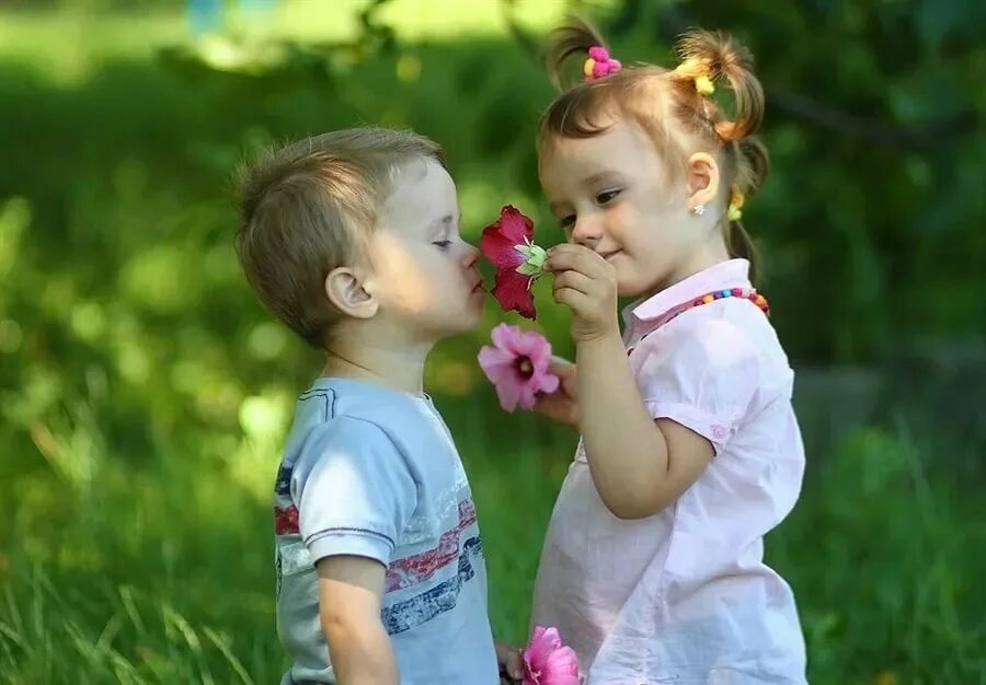 Счастливый ребенок. Мальчик дарит девочке цветы. Счастливое детство. Мальчик и девочка смеются.