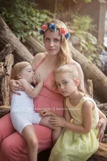 Woman sits breastfeeding three year old daughter beside older daughter. 