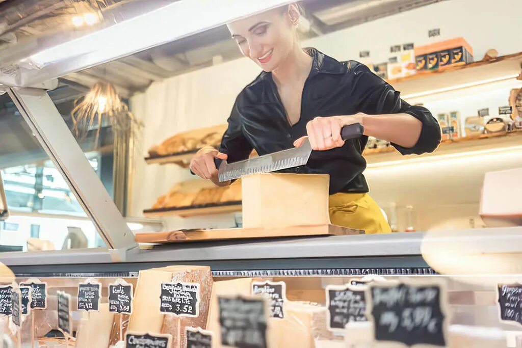 Головка сыра с вырезанным куском. Сыр разрезанный. Голова ремесленного сыра. Продавец режет сыр. Сыр порезанный.