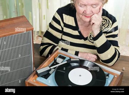 The elderly woman sitting at the table and listening to music retro from a ...