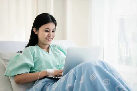 patient lying in a hospital bed using a laptop.