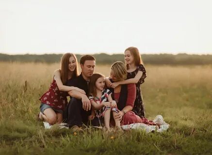 a group of people sitting on top of a grass covered field next to each othe...