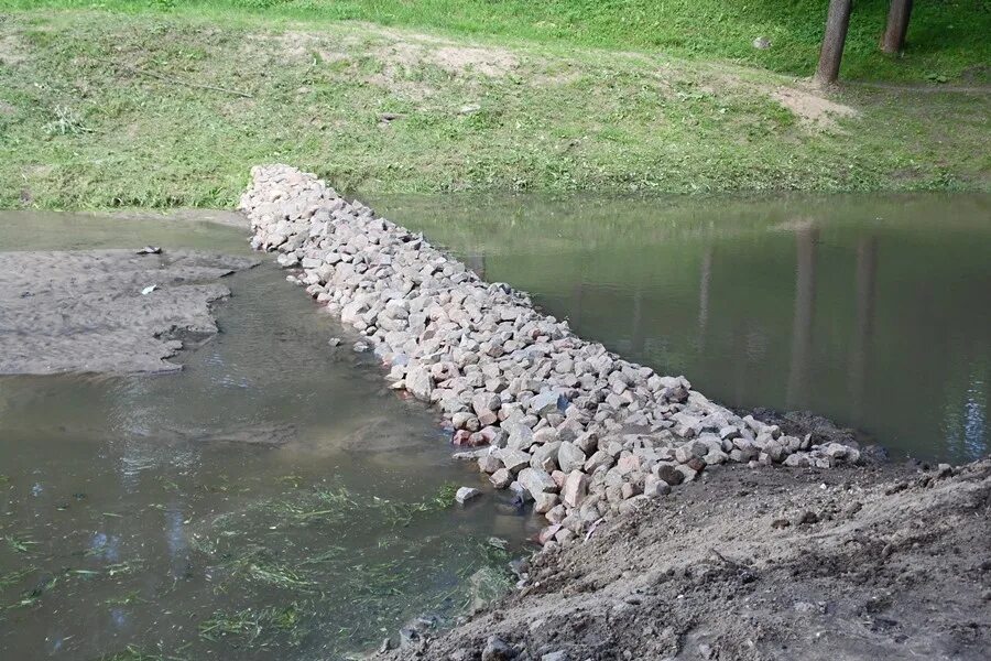 Люди перегородили реку большой плотиной вода. Запруда из камней. Каменная запруда на ручье. Дамба на ручье. Плотина из камня.