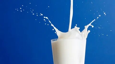 Glass Of Milk Splashing Over Blue Background Wallpaper.