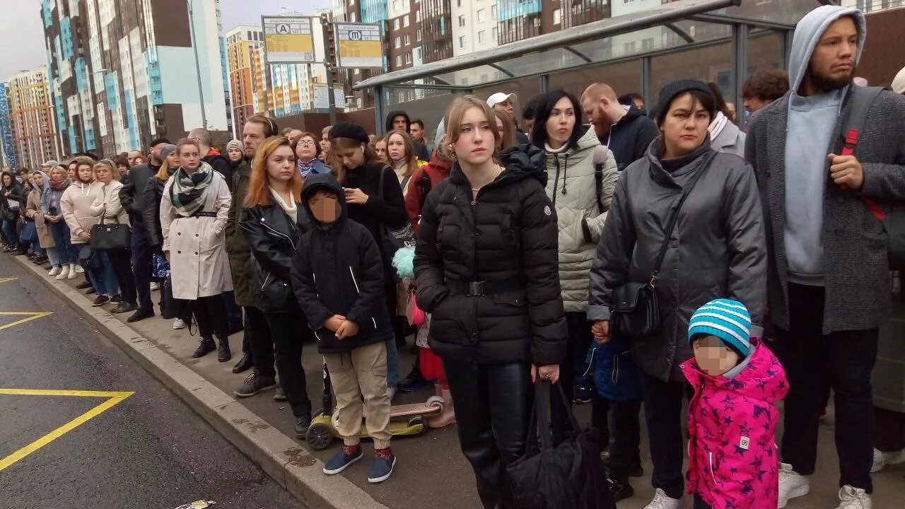 Люди ждут автобус на остановке. Санкт-Петербург Арцеуловская аллея. Толпа людей на остановке. Очередь на остановке в Питере. Толпа на остановке в Мурино.