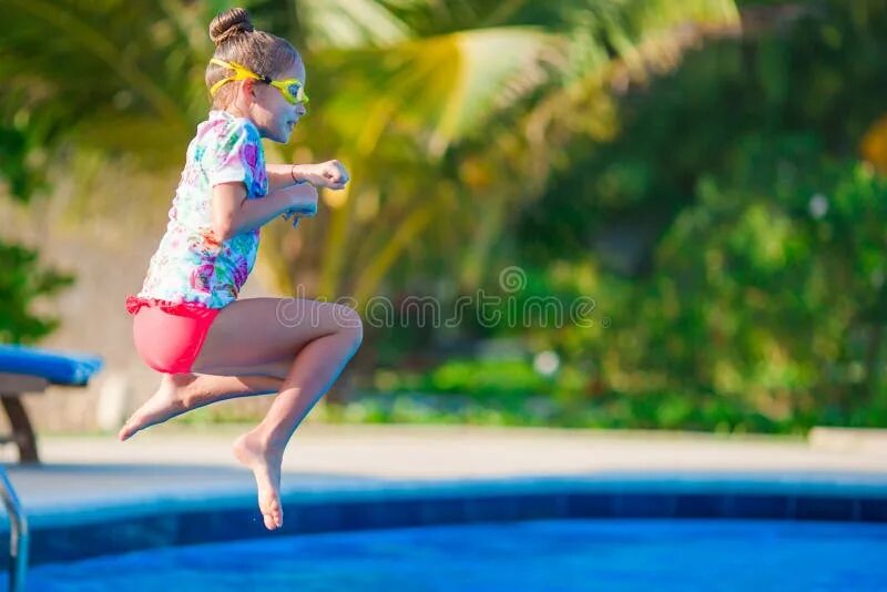 Девочка прыгает в бассейн. Маленькая девочка прыгает в бассейн. Красивая маленькая девочка развлекается у открытого бассейна.