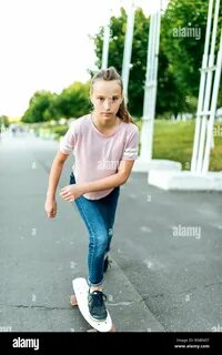 Teenager girl 10-12 years old, in the summer in the city, riding a skateboa...