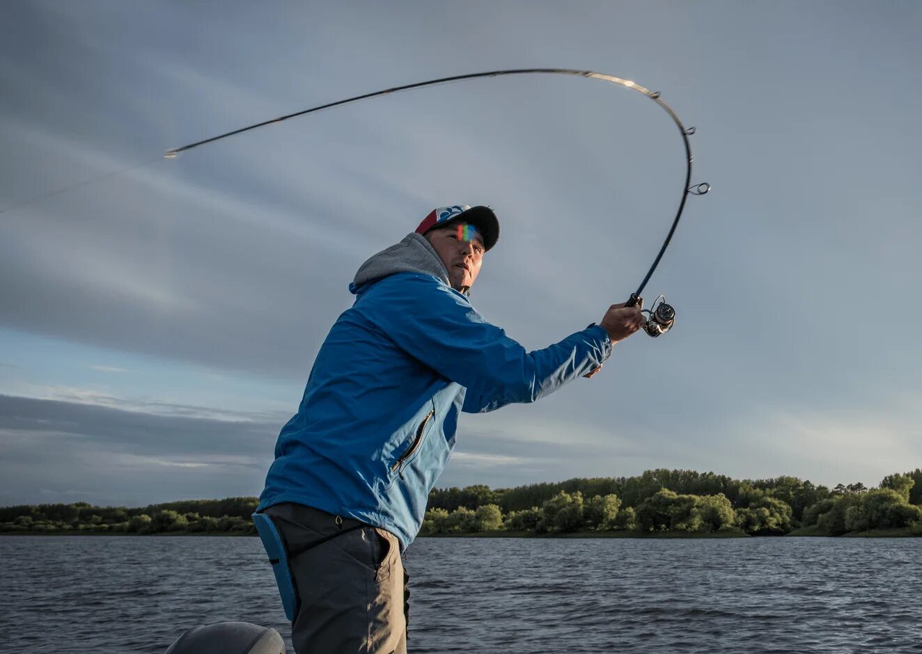 Рыбкой тянет. Вываживание крупной рыбы. Красивый спиннинг. Рыбак со спиннингом. Рыбак на рыбалке.