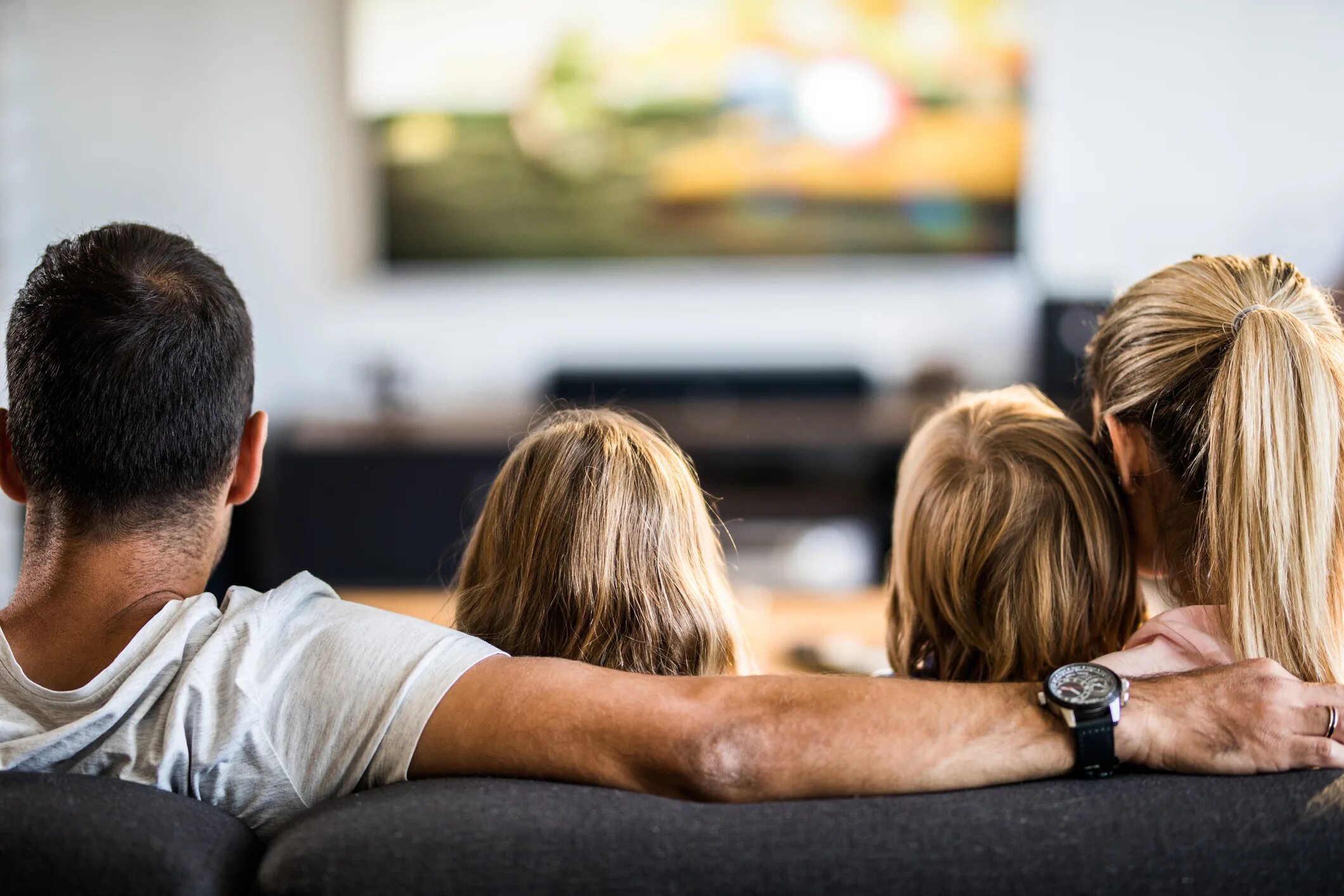 Семья на диване перед телевизором. Семья смотрит телевизор.