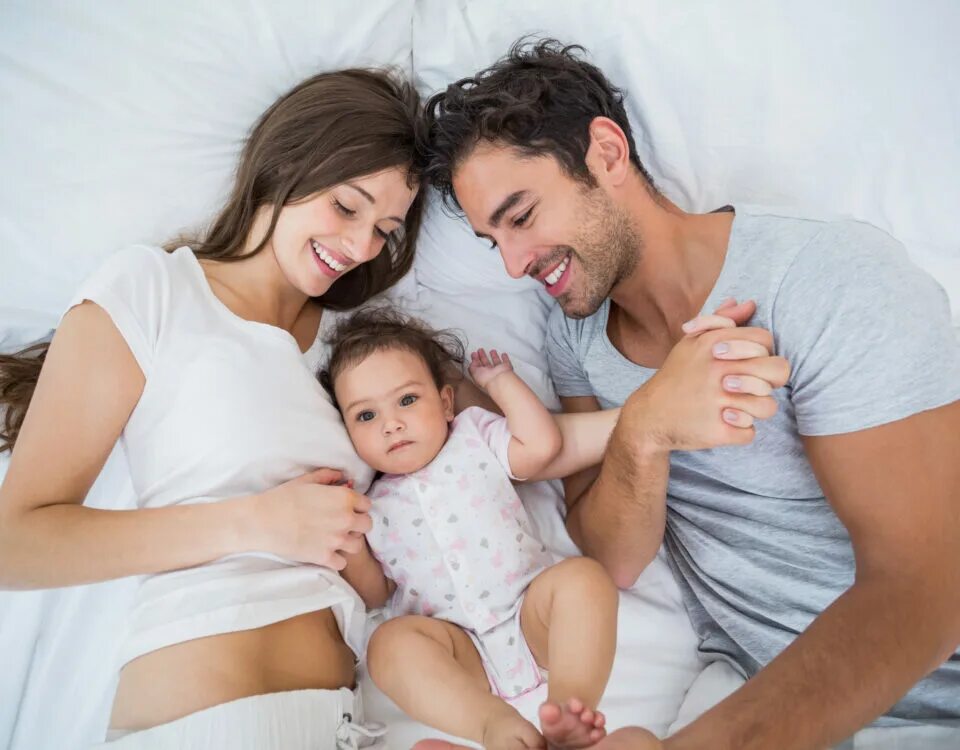 Семья на кровати. Счастливая семья у кроватки новорожденного. Семья лежит на кровати. Счастливая семья в кровати картинки хорошего качества.