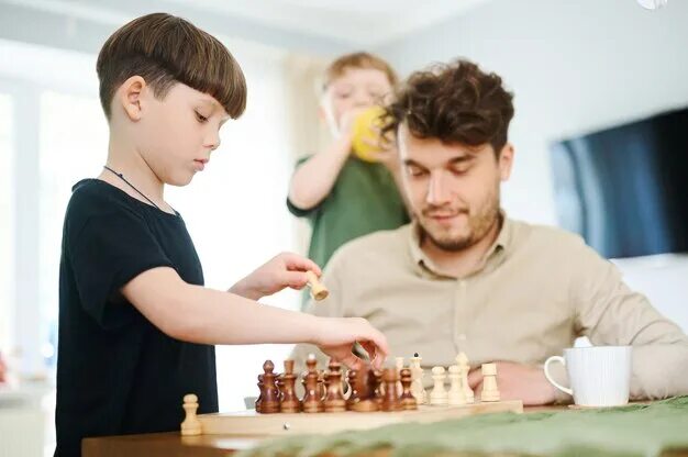 Папа учит играть в шахматы. Отец обучает шахматам. Папа учит сына шахматам. Отец и сын играют в шахматы. Научи папу играть