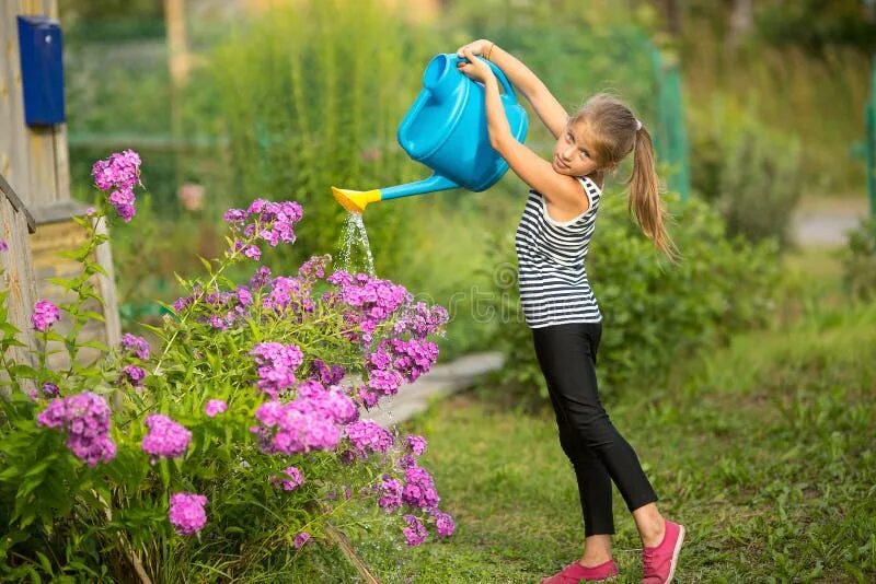 Девочка поливает клумбу. Девушка поливает цветы в саду. She to water the flowers. Девочка поливает цветы. Девочка с лейкой.