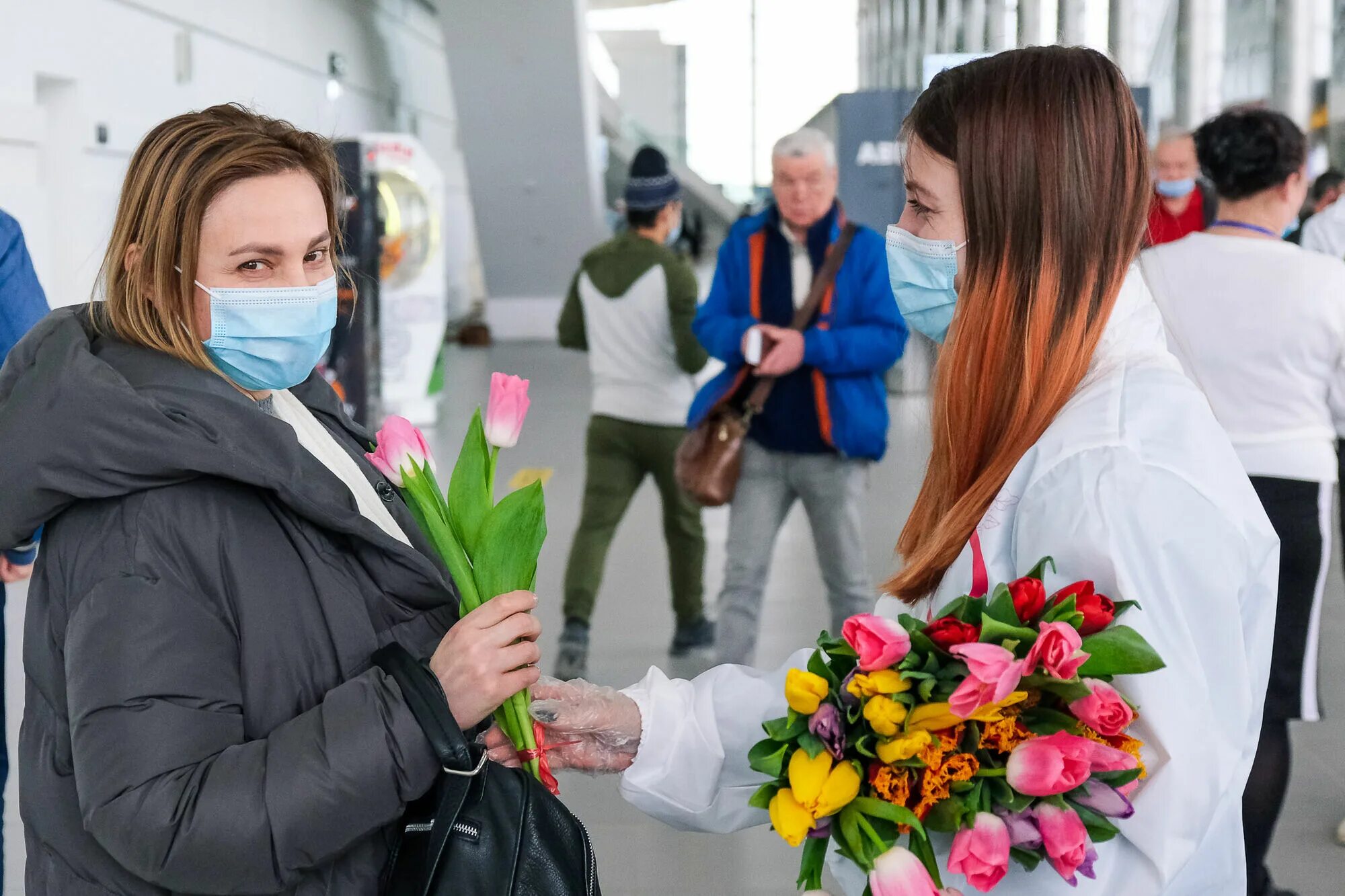 Волонтеры цветы. Встречает с цветами. Встречает в аэропорту с цветами. Волонтеры встречают в аэропорту. Встреча девушки в аэропорту с цветами.