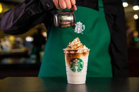 a starbucks employee pours coffee into a cup with whipped cream on top and ...