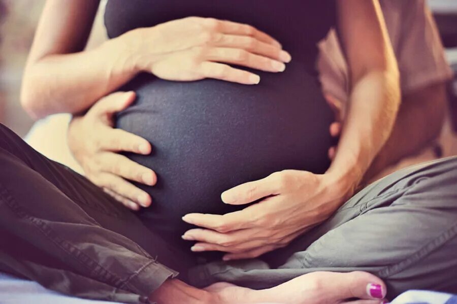 Обнять беременную. Мужские руки на беременном животе.