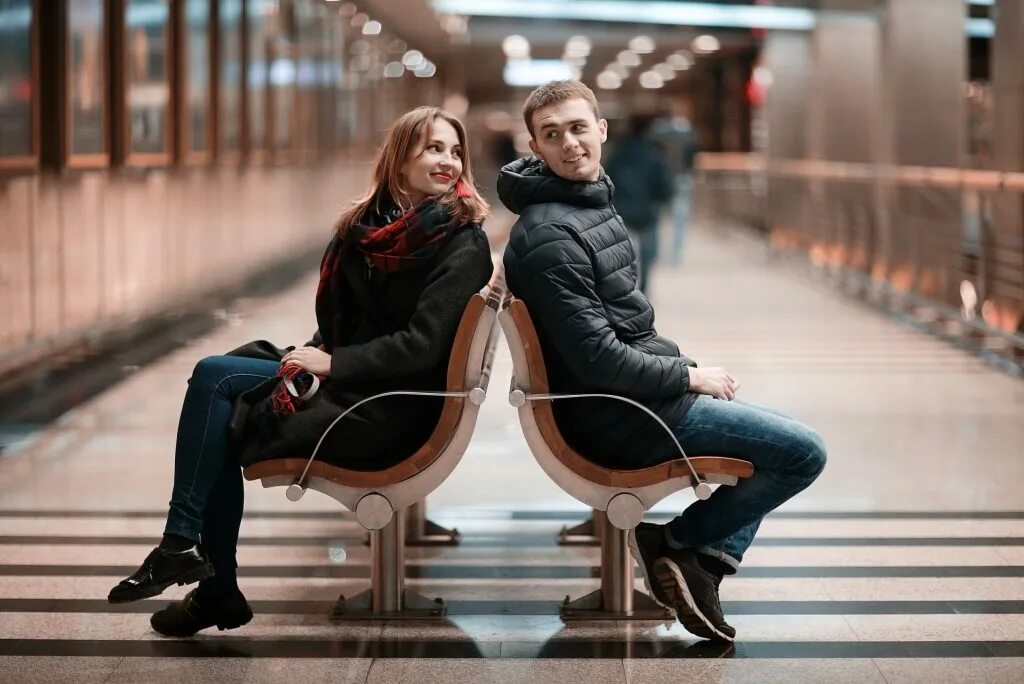 Где назначить свидание. Man and woman sitting. Парочка сидит девушка в платье сидит среди толпы. Woman sitting on Chair and man Stan behind.