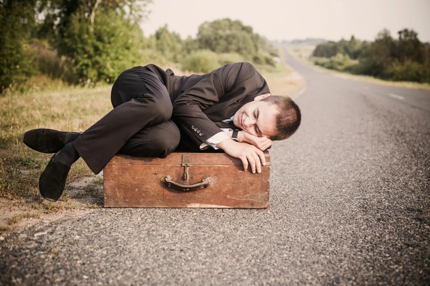 Устал от долгой дороги. Мужик с чемоданом. Мужчина лежит. Мужчина с чемоданом на дороге.