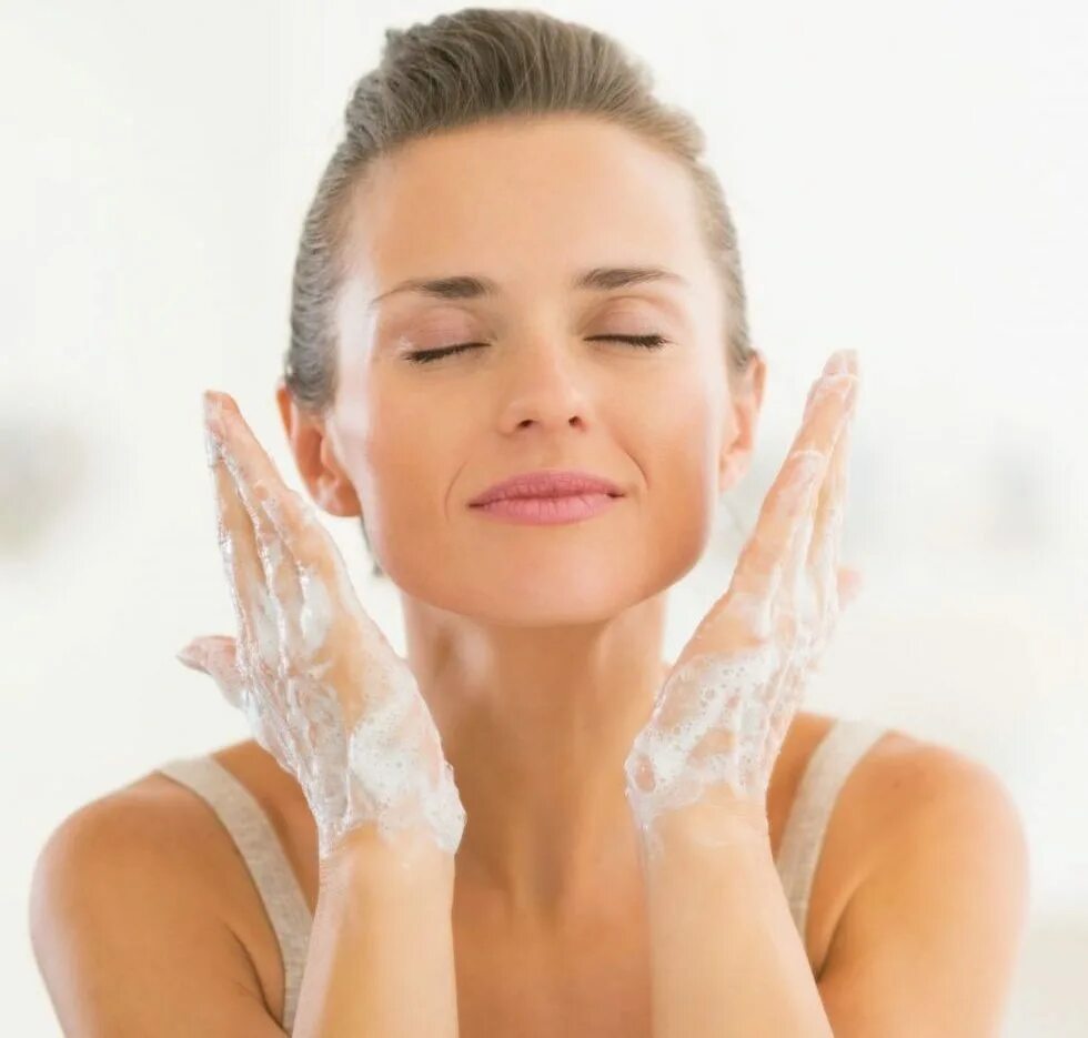 Девушка умывается. Очищение лица. Умывать лицо. Лицо девушки на белом фоне. Забота о коже лица.