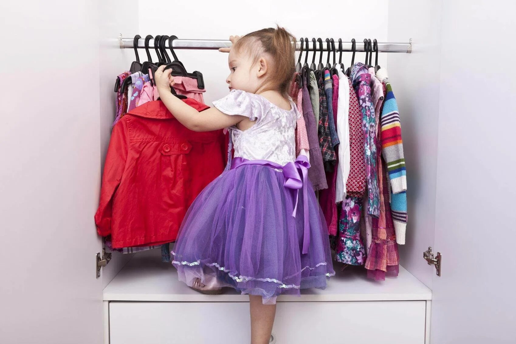 Детская одежда на вешалке. Много одежды на ребенке. Дети примеряют одежду. Выбор одежды для детей.