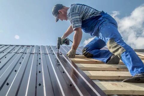 male builder performs work on the roof, fastens corrugated sheets.