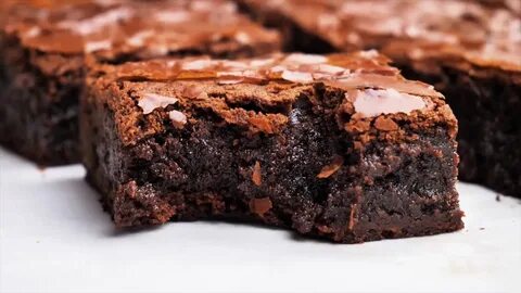 chocolate brownies with icing on top are sitting on a white surface and rea...
