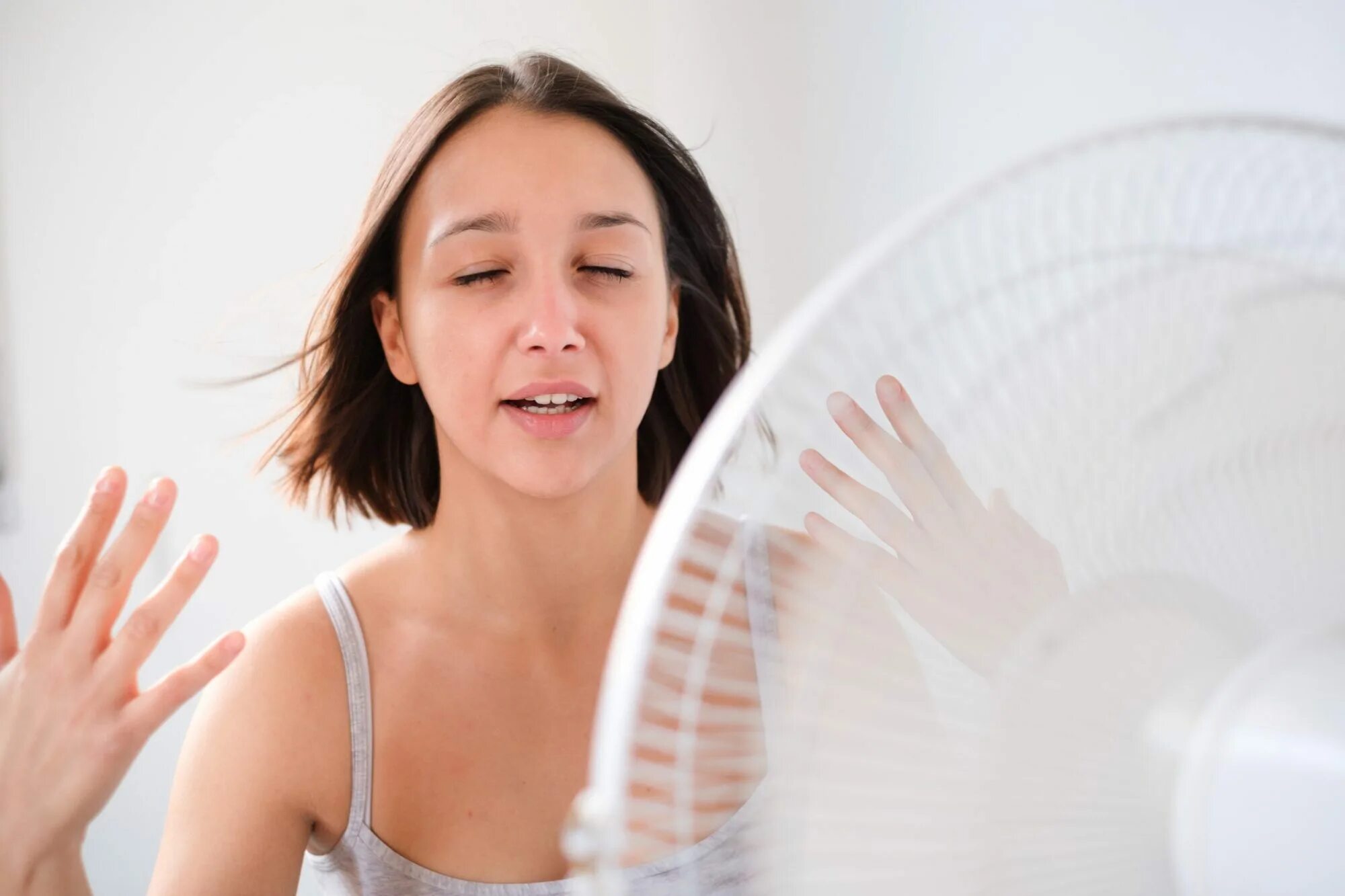 Слабость после жары. Сильная потливость летом. Человек-вентилятор. Женщина потеет. Девушка перед вентилятором.