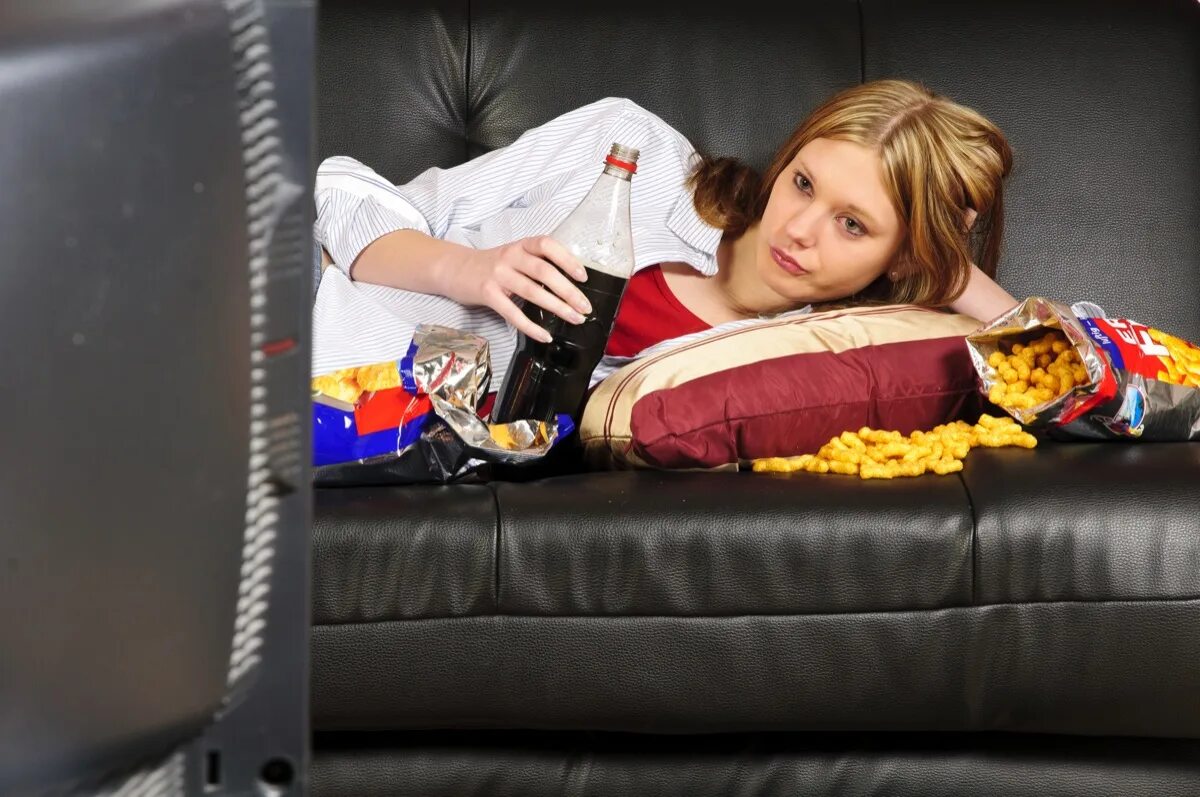 Диван перед телевизором. Женщина перед телевизором. Ленивая девушка. Женщина лежит на диване. Девушка лежит на диване с чипсами.