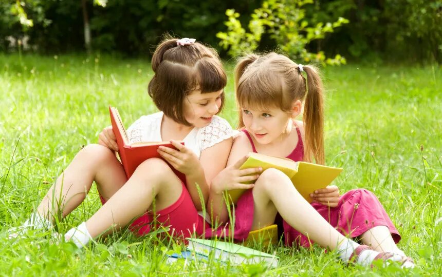 Reading girls Pink. Little in skirt on grass. Two girls Lie on the grass and talk. Two girls sitting on the Lawn. Little girl sisters