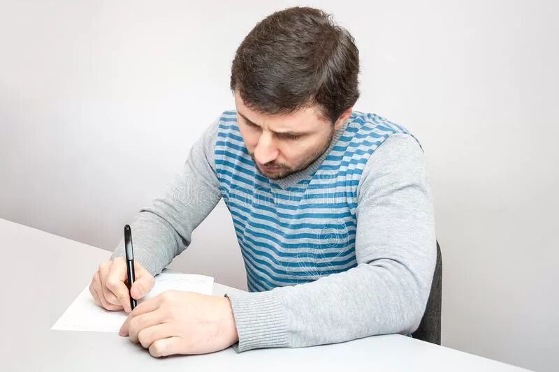 Человек сидит за столом. Люди сидят за столом в офисе. Мужчина думает за столом. Человек что-то пишет. Сидящий человек пишет.