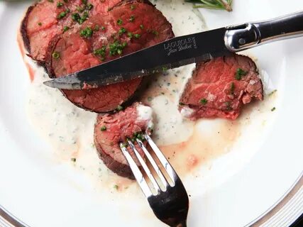 Fork and knife alongside sliced beef tenderloin medallions on a horseradish...
