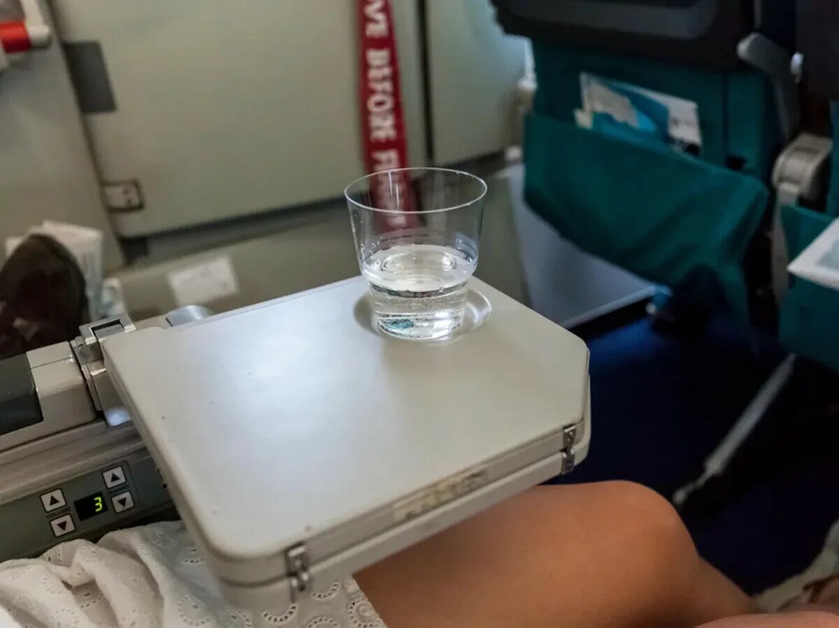 Воду на борт самолета. Стаканчики в самолете. Стакан с водой в самолёт. Обезвоживание в самолете. Девушка пьет воду в самолете.